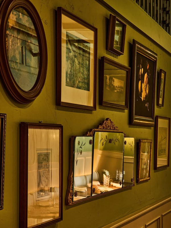 Collection of framed pictures and mirrors on a green wall
