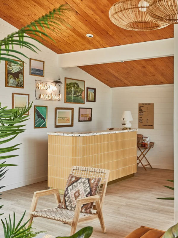Modern interior with wooden reception desk, armchair, and framed artwork on a white wall.