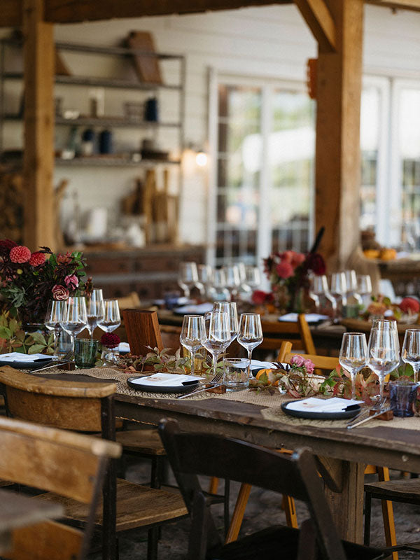 Dining table set with wine glasses, plates, and flowers in a rustic setting.