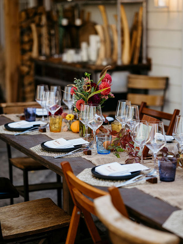 Dining table set with glasses, plates, and a floral centerpiece in a rustic setting.