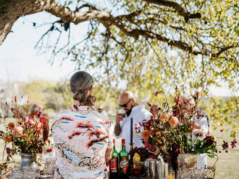 People getting drinks at an outdoor table with floral arrangements under a tree