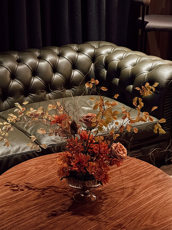 Decorative flowers in a vase on a wooden table with a leather sofa in the background.