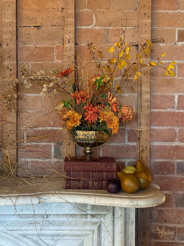 Decorative arrangement with flowers, books, and pears on a marble ledge against a brick wall.
