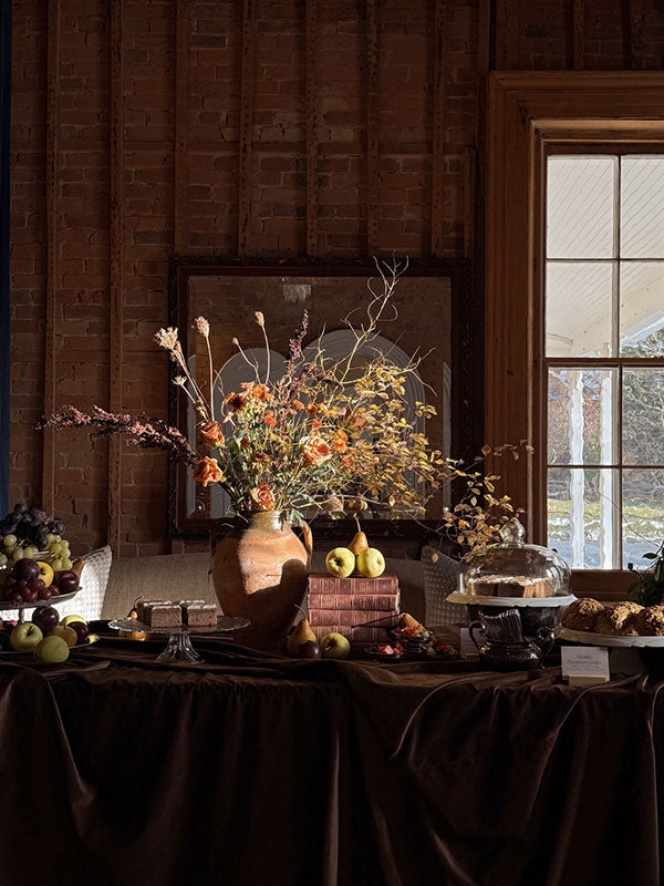 Decorative table setting with flowers, fruits, and a window in the background.