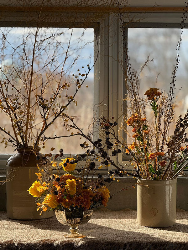 Decorative arrangement of flowers and branches in vases on a windowsill.