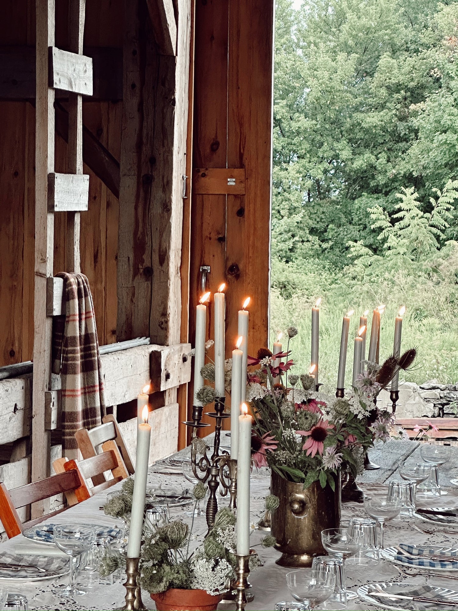 Dining table set with candles, flowers, and glasses in a rustic wooden cabin setting.