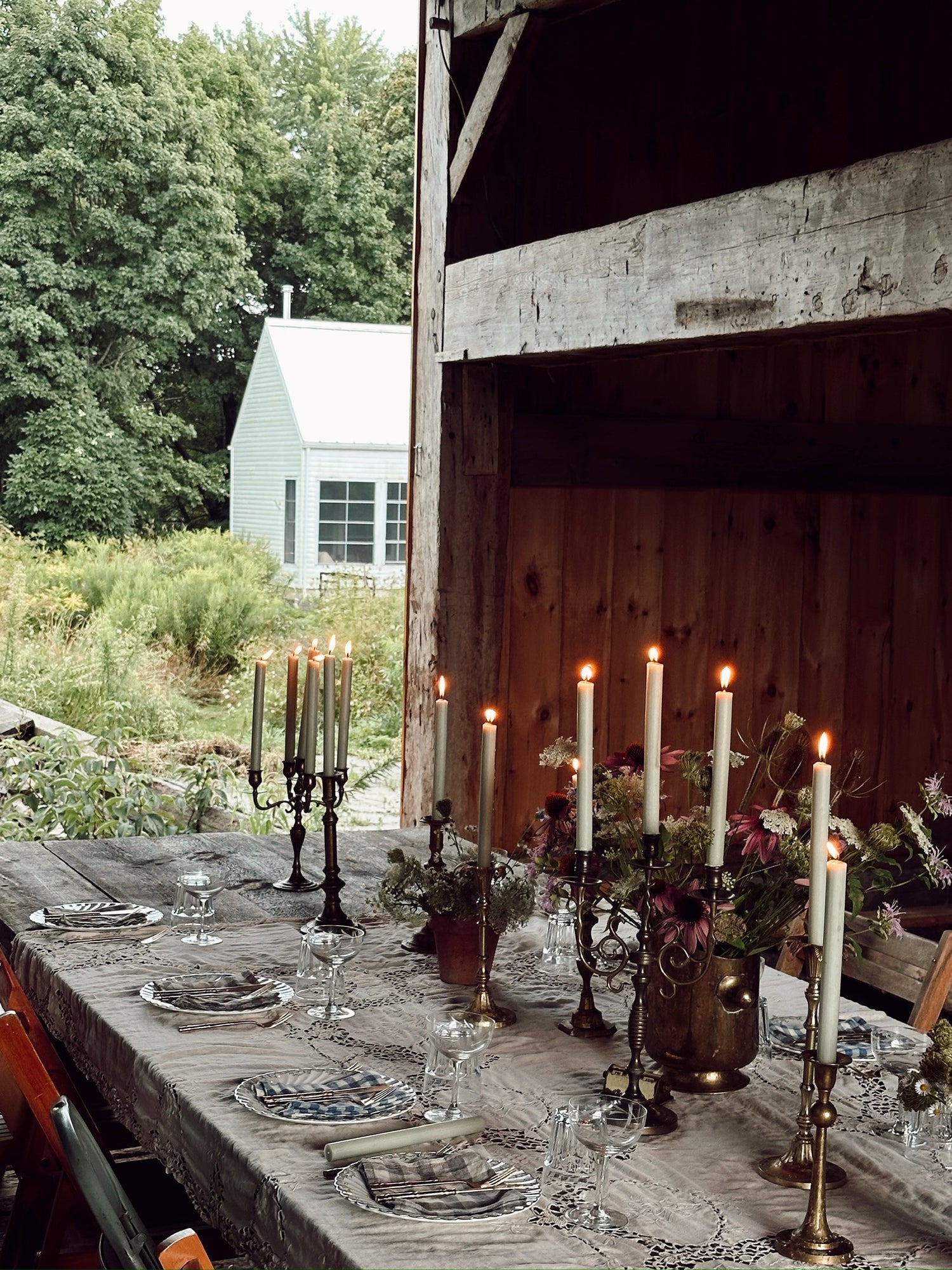 Dining table set with candles and plates outdoors near a wooden building.