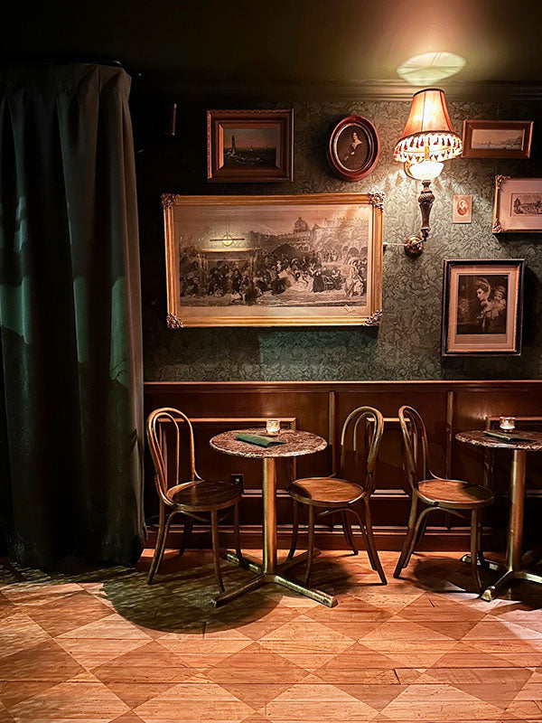 Vintage-style bar with wooden floors, round tables, and framed pictures on the wall.