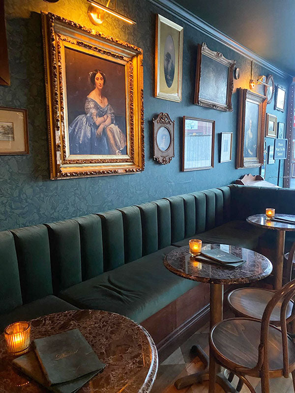 Decorative interior of a bar or restaurant with green velvet booths, framed pictures on the wall, and candles on tables.