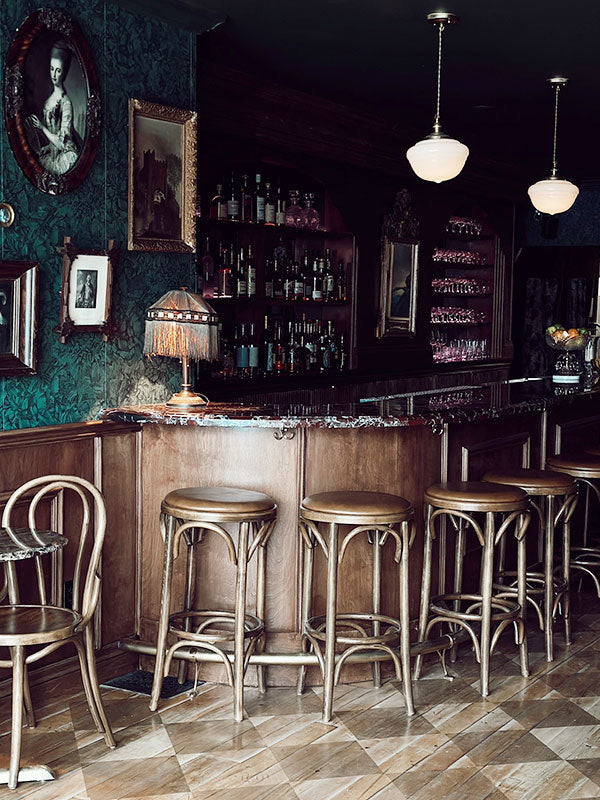 Bar interior with wooden bar, stools, and framed pictures on a dark wall.