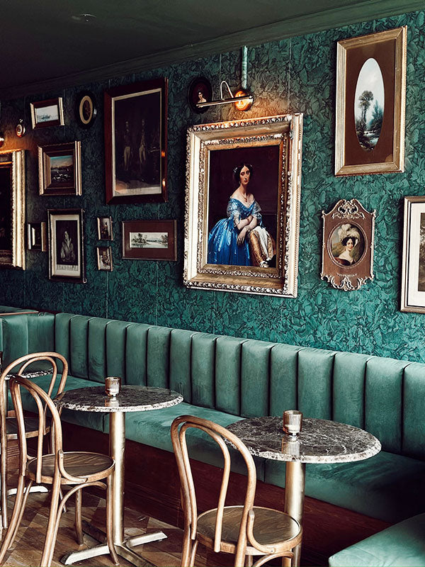 Decorative interior of a restaurant with green walls, framed pictures, and wooden chairs.
