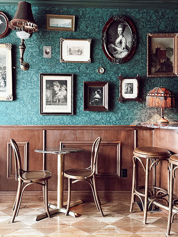Vintage-style interior with green wallpaper, framed pictures, wooden furniture, and a small table.