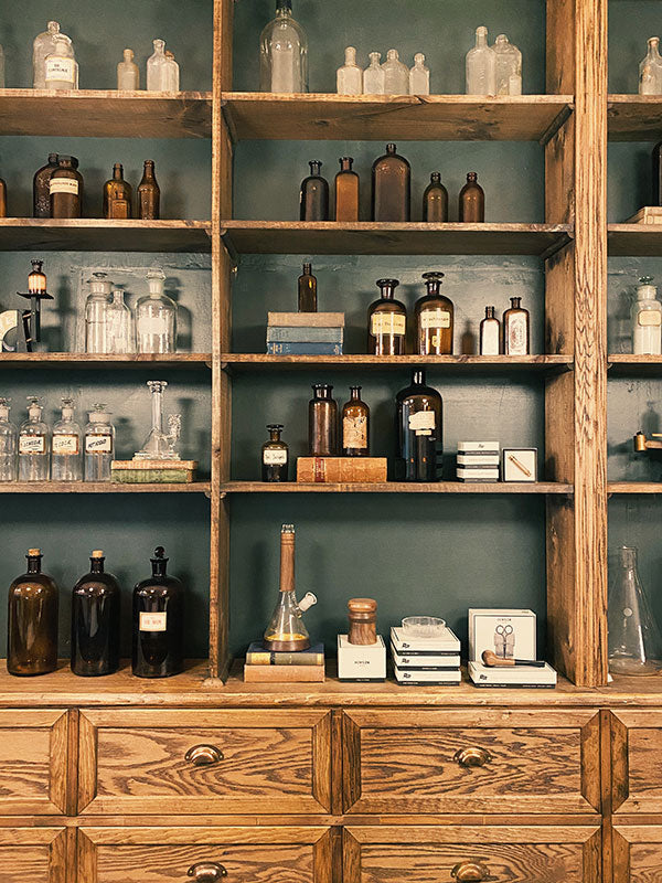 Wooden shelves with various bottles and jars against a green wall.