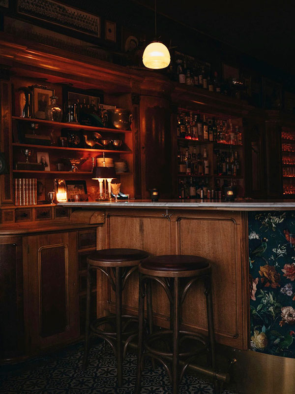 Dark bar with wooden shelves, stools, and a hanging light bulb.