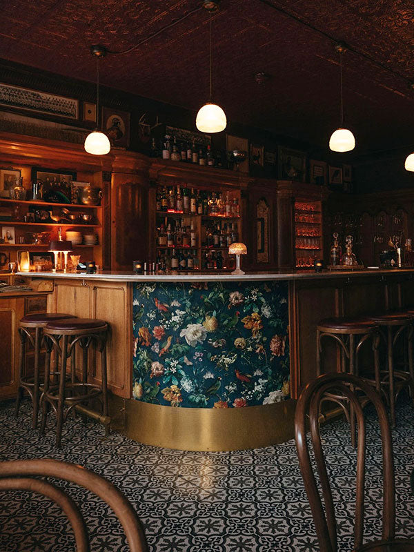 Dark interior of a bar with floral-patterned bar front and wooden chairs.
