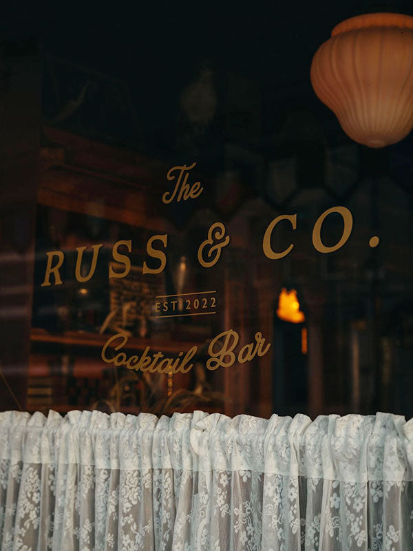 Glass window with 'The Russ & Co. Cocktail Bar' sign.