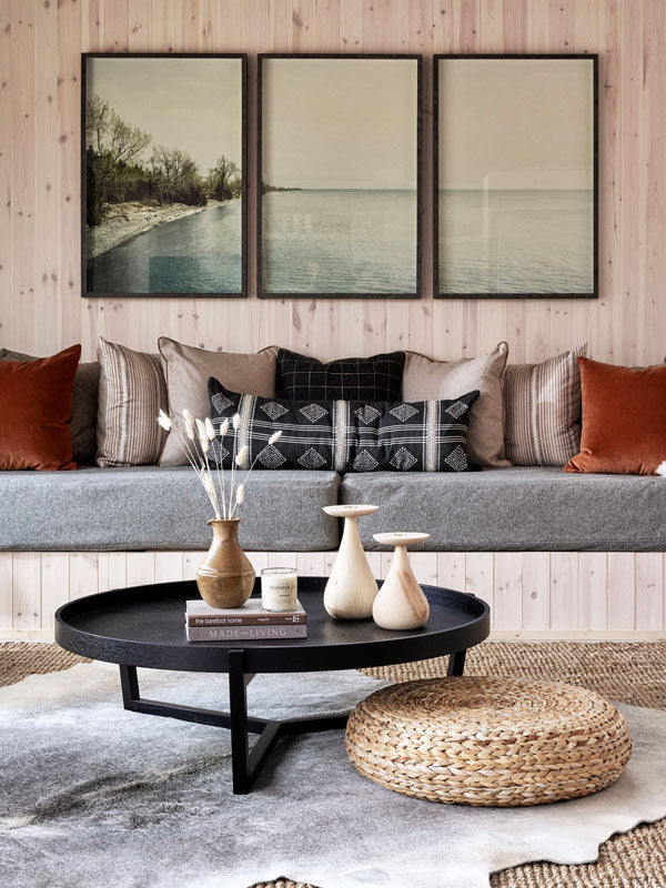 Living room with a gray sofa, round black coffee table, and wall art depicting a landscape.